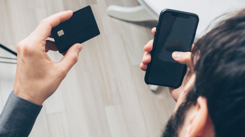 Pessoa segurando cartão de crédito e celular para uma compra online