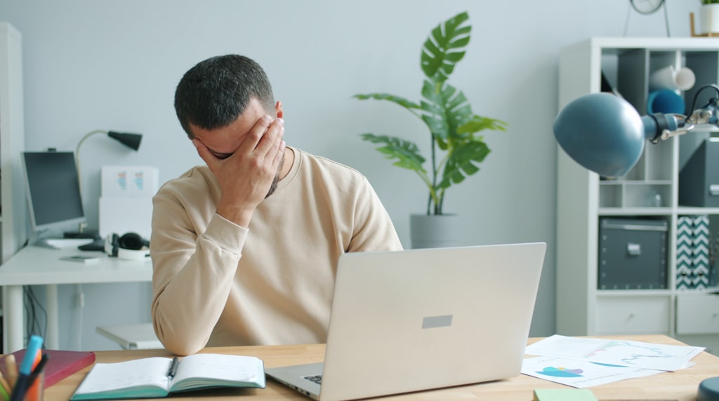 Homem frustrado esfregando o rosto diante do laptop
