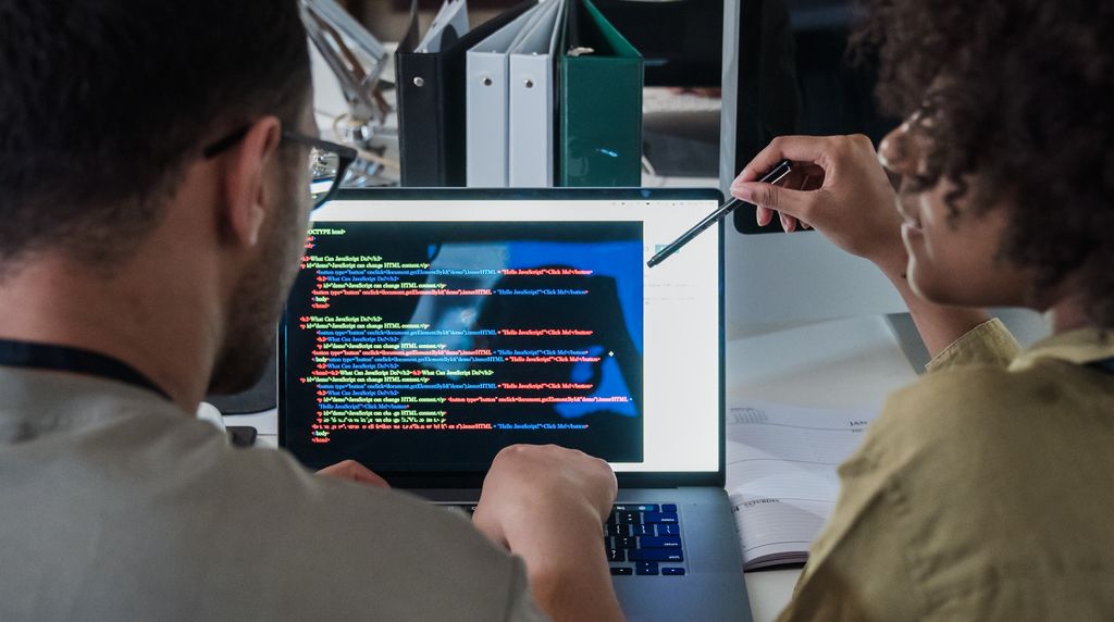 Dois desenvolvedores programando em um laptop em um escritório moderno