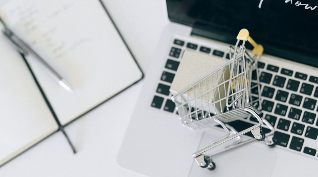 Mini carrinho de compras sobre um laptop, representando dados de produto no e-commerce