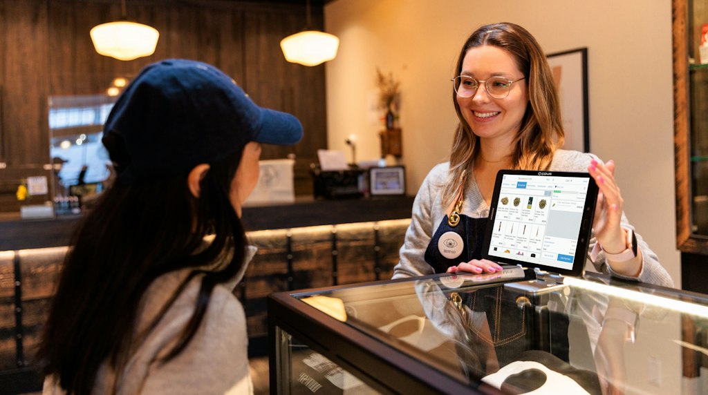 Atendente mostrando informacoes em um tablet para uma cliente no balcao da loja