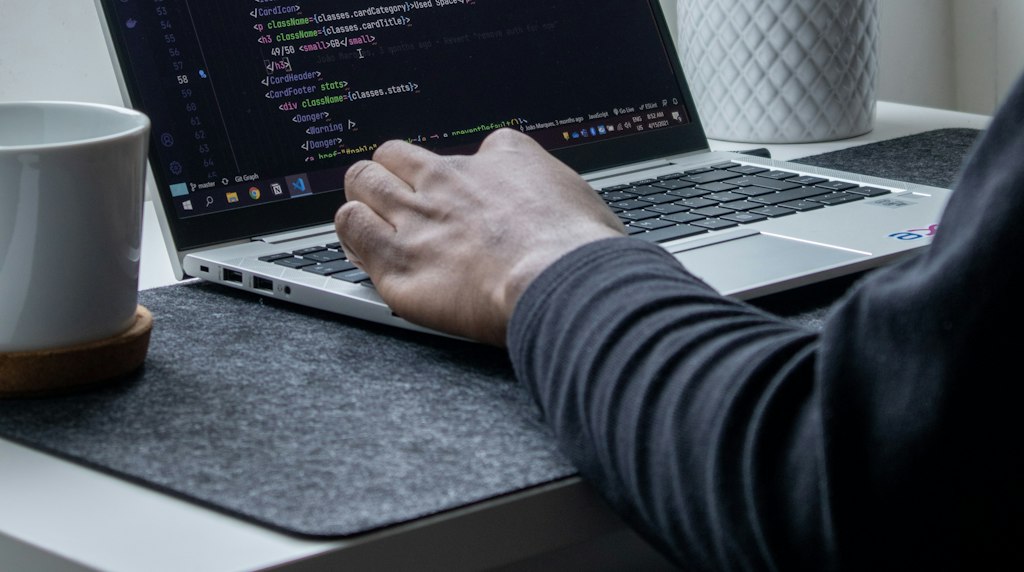 Pessoa digitando código em um laptop, com xícara de café ao lado, representando trabalho diário com modelos de IA