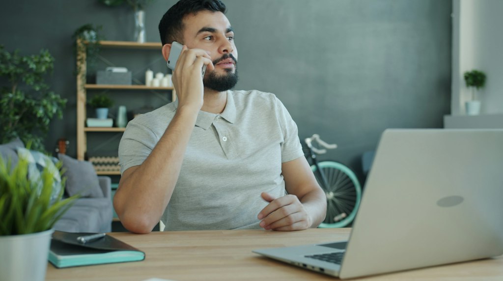 Cliente ao telefone na mesa com o notebook aberto, aguardando atendimento