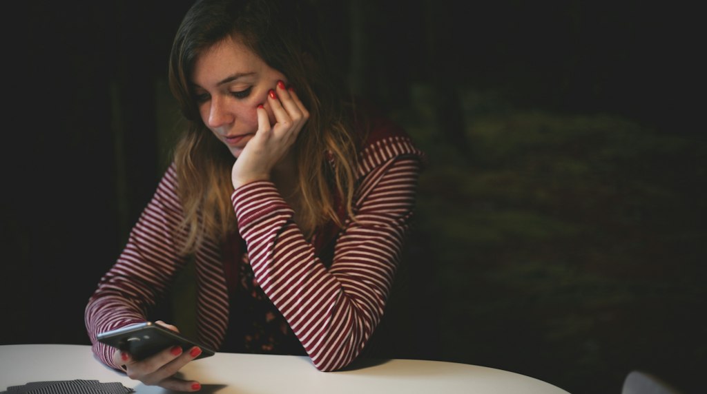 Mulher apoiada na mesa olhando sem interesse para o celular