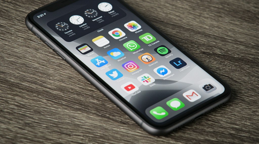 Smartphone apoiado em superfície de madeira com a tela inicial cheia de ícones de aplicativos
