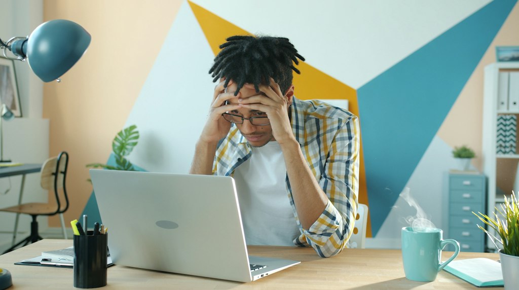 Homem com as maos na cabeca em frustracao diante de um notebook