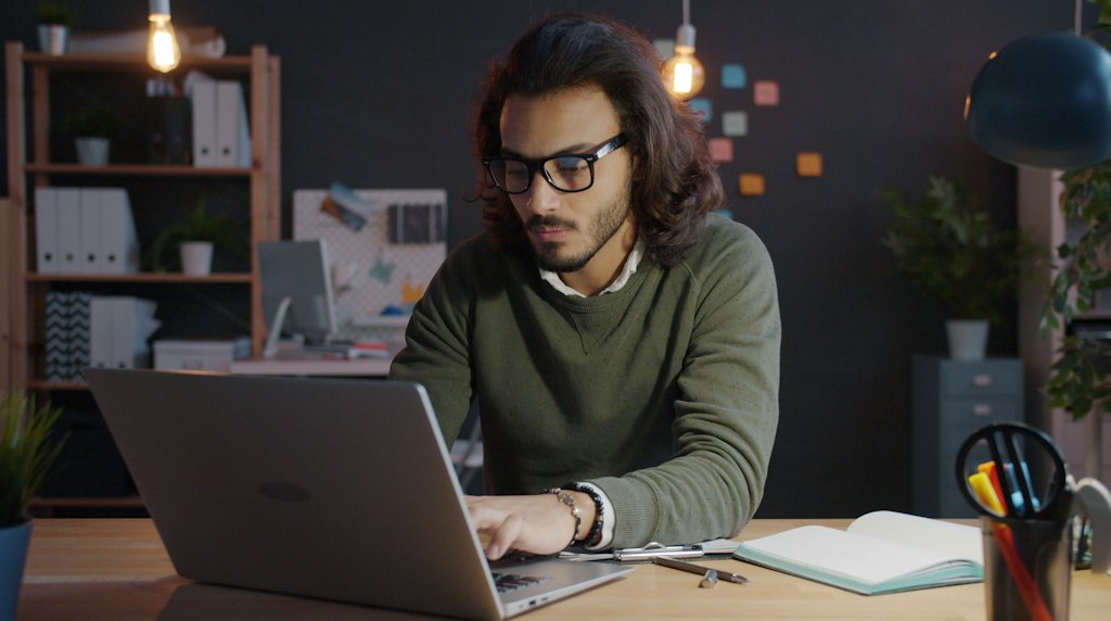 Profissional de midia analisando sozinho uma campanha no laptop em escritorio com pouca luz