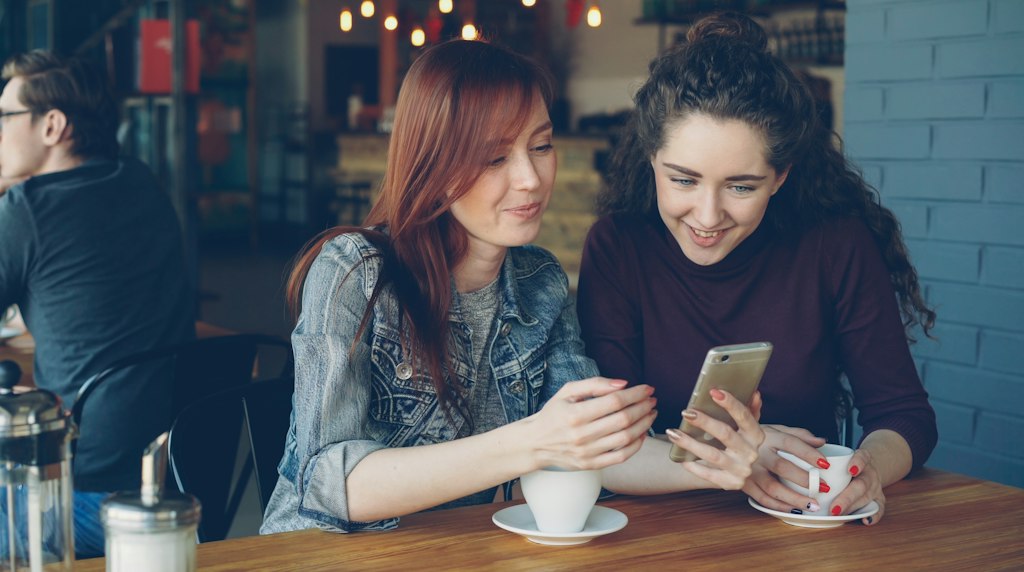 Duas pessoas em um cafe olhando juntas a tela de um celular