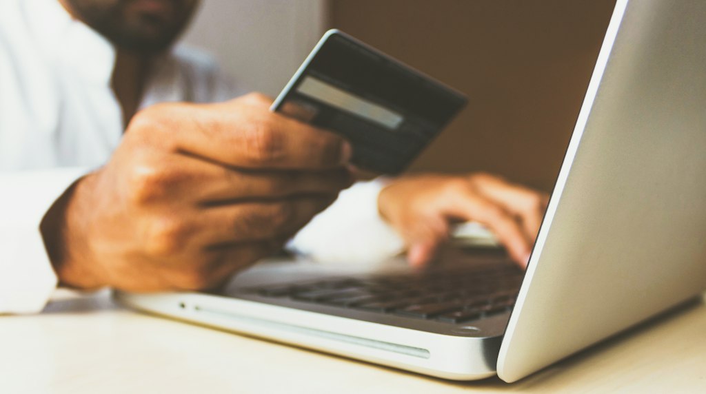 Pessoa usando notebook e segurando cartao de credito durante compra online