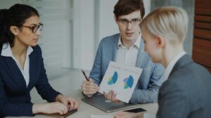 Tres profissionais analisando graficos durante uma reuniao comercial