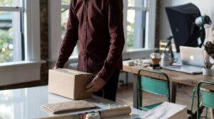 Pessoa segurando uma caixa de papelão sobre uma mesa, representando o pedido de um cliente após a compra